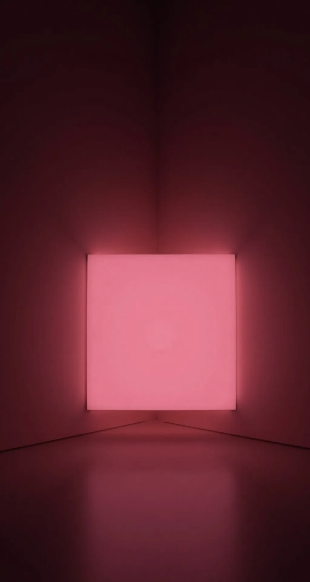 A soft pink light cube floating in the corner of a dark room.