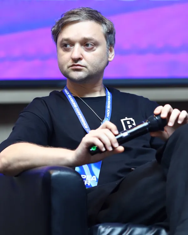 Igor Pugachevsky on a conference panel in a black Blum T-shirt, holding a microphone.